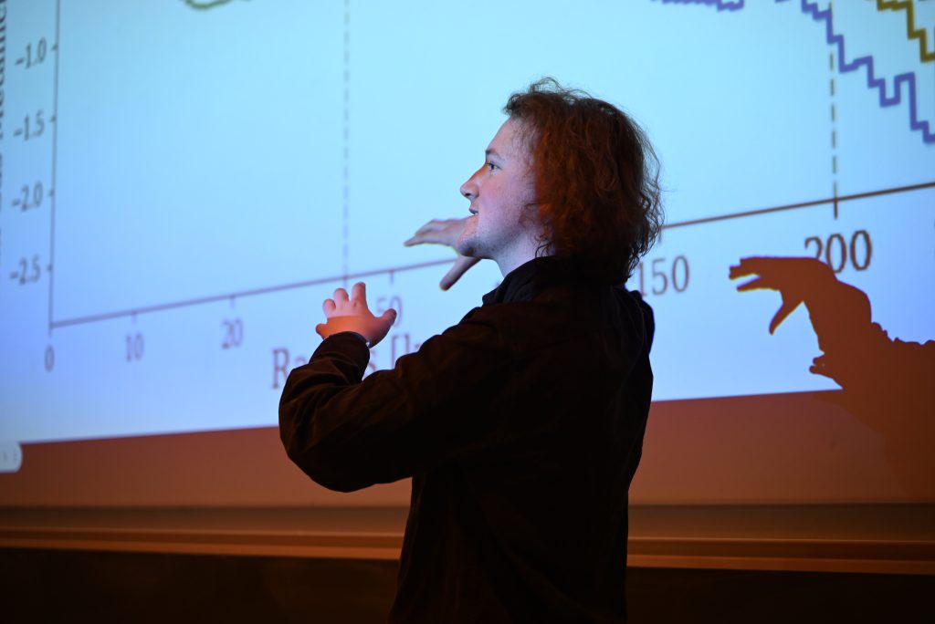 conf26_studentlecture A person standing in front of a projection of a graph. The graph is not clearly visible, but he is gesturing towards it.